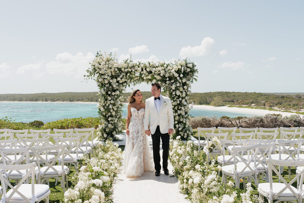 Lush and romantic ceremony chuppah florals for beachfront wedding in the Bahamas. The chuppah highlights garden roses, hydrangeas, delphinium, spray roses, baby’s breath, chrysanthemums, oncidium, wisteria, tulips and a mixture of airy greens to create an elegant and dramatic focal point. Layered textures and soft movement blend seamlessly with lush aisle meadows featuring the same flowers as the chuppah. Design by Rosemary & Finch Floral Design in Nashville, TN.