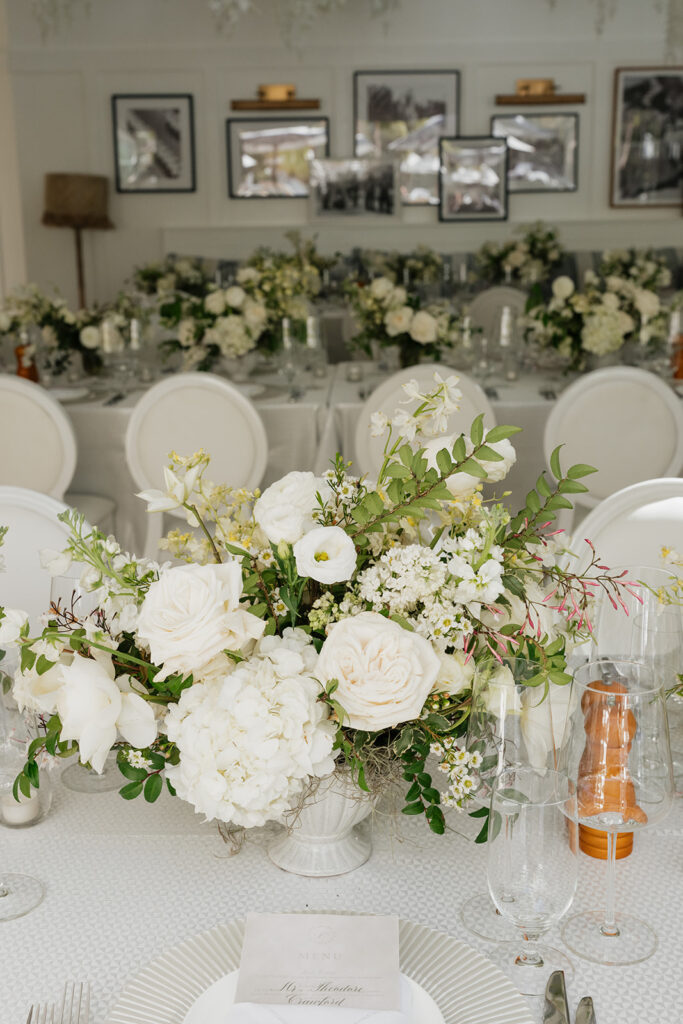 Ethereal white wedding reception with a breathtaking canopy of cascading white wisteria & green vines. Tables feature low, lush centerpieces combining garden roses, hydrangeas, spray roses, waxflower, delphinium, ranunculus, tulips, oncidium orchids, lisianthus, tweedia, lilac, sweet peas and are accented by deep-green foliage. This stunning floral design creates a luxurious, romantic, all-white atmosphere. Design by Rosemary & Finch Floral Design in Nashville, TN. 