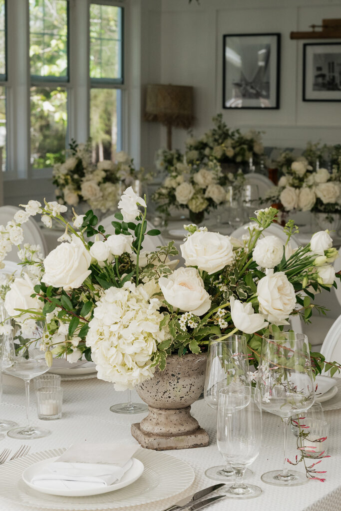 Ethereal white wedding reception with a breathtaking canopy of cascading white wisteria & green vines. Tables feature low, lush centerpieces combining garden roses, hydrangeas, spray roses, waxflower, delphinium, ranunculus, tulips, oncidium orchids, lisianthus, tweedia, lilac, sweet peas and are accented by deep-green foliage. This stunning floral design creates a luxurious, romantic, all-white atmosphere. Design by Rosemary & Finch Floral Design in Nashville, TN. 