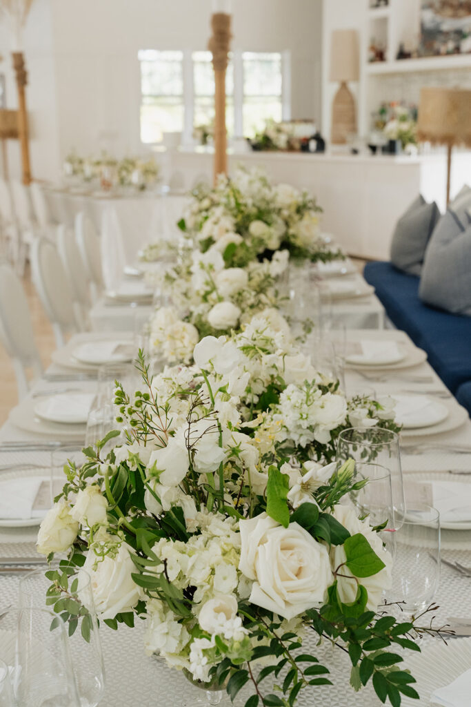 Ethereal white wedding reception with a breathtaking canopy of cascading white wisteria & green vines. Tables feature low, lush centerpieces combining garden roses, hydrangeas, spray roses, waxflower, delphinium, ranunculus, tulips, oncidium orchids, lisianthus, tweedia, lilac, sweet peas and are accented by deep-green foliage. This stunning floral design creates a luxurious, romantic, all-white atmosphere. Design by Rosemary & Finch Floral Design in Nashville, TN. 