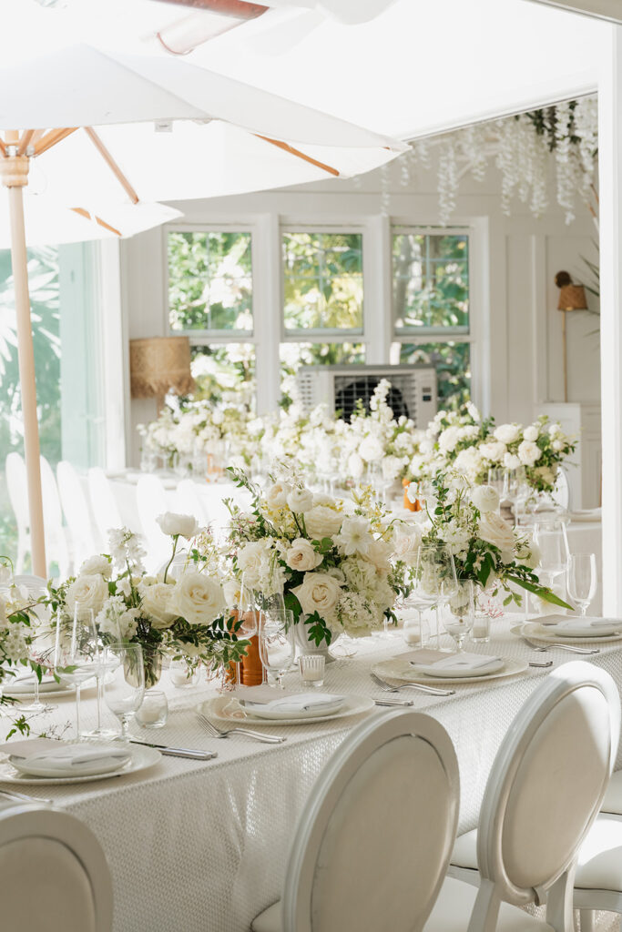 Ethereal white wedding reception with a breathtaking canopy of cascading white wisteria & green vines. Tables feature low, lush centerpieces combining garden roses, hydrangeas, spray roses, waxflower, delphinium, ranunculus, tulips, oncidium orchids, lisianthus, tweedia, lilac, sweet peas and are accented by deep-green foliage. This stunning floral design creates a luxurious, romantic, all-white atmosphere. Design by Rosemary & Finch Floral Design in Nashville, TN. 