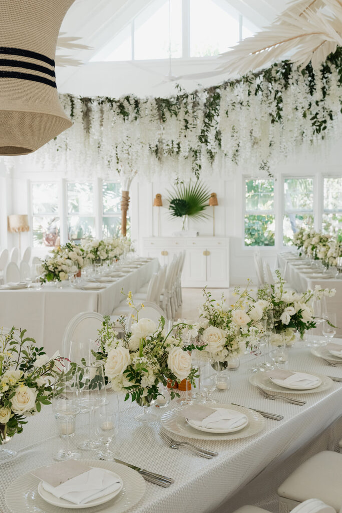 Ethereal white wedding reception with a breathtaking canopy of cascading white wisteria & green vines. Tables feature low, lush centerpieces combining garden roses, hydrangeas, spray roses, waxflower, delphinium, ranunculus, tulips, oncidium orchids, lisianthus, tweedia, lilac, sweet peas and are accented by deep-green foliage. This stunning floral design creates a luxurious, romantic, all-white atmosphere. Design by Rosemary & Finch Floral Design in Nashville, TN. 
