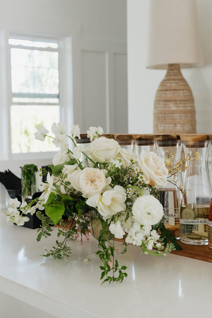 Ethereal white wedding reception with a breathtaking canopy of cascading white wisteria & green vines. Tables feature low, lush centerpieces combining garden roses, hydrangeas, spray roses, waxflower, delphinium, ranunculus, tulips, oncidium orchids, lisianthus, tweedia, lilac, sweet peas and are accented by deep-green foliage. This stunning floral design creates a luxurious, romantic, all-white atmosphere. Design by Rosemary & Finch Floral Design in Nashville, TN. 