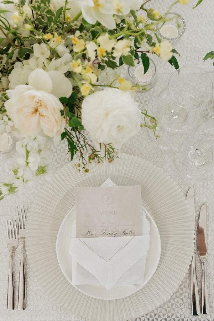 Ethereal white wedding reception with a breathtaking canopy of cascading white wisteria & green vines. Tables feature low, lush centerpieces combining garden roses, hydrangeas, spray roses, waxflower, delphinium, ranunculus, tulips, oncidium orchids, lisianthus, tweedia, lilac, sweet peas and are accented by deep-green foliage. This stunning floral design creates a luxurious, romantic, all-white atmosphere. Design by Rosemary & Finch Floral Design in Nashville, TN. 