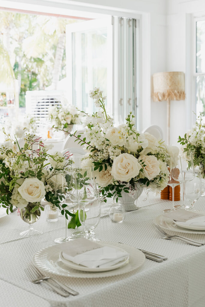 Ethereal white wedding reception with a breathtaking canopy of cascading white wisteria & green vines. Tables feature low, lush centerpieces combining garden roses, hydrangeas, spray roses, waxflower, delphinium, ranunculus, tulips, oncidium orchids, lisianthus, tweedia, lilac, sweet peas and are accented by deep-green foliage. This stunning floral design creates a luxurious, romantic, all-white atmosphere. Design by Rosemary & Finch Floral Design in Nashville, TN. 