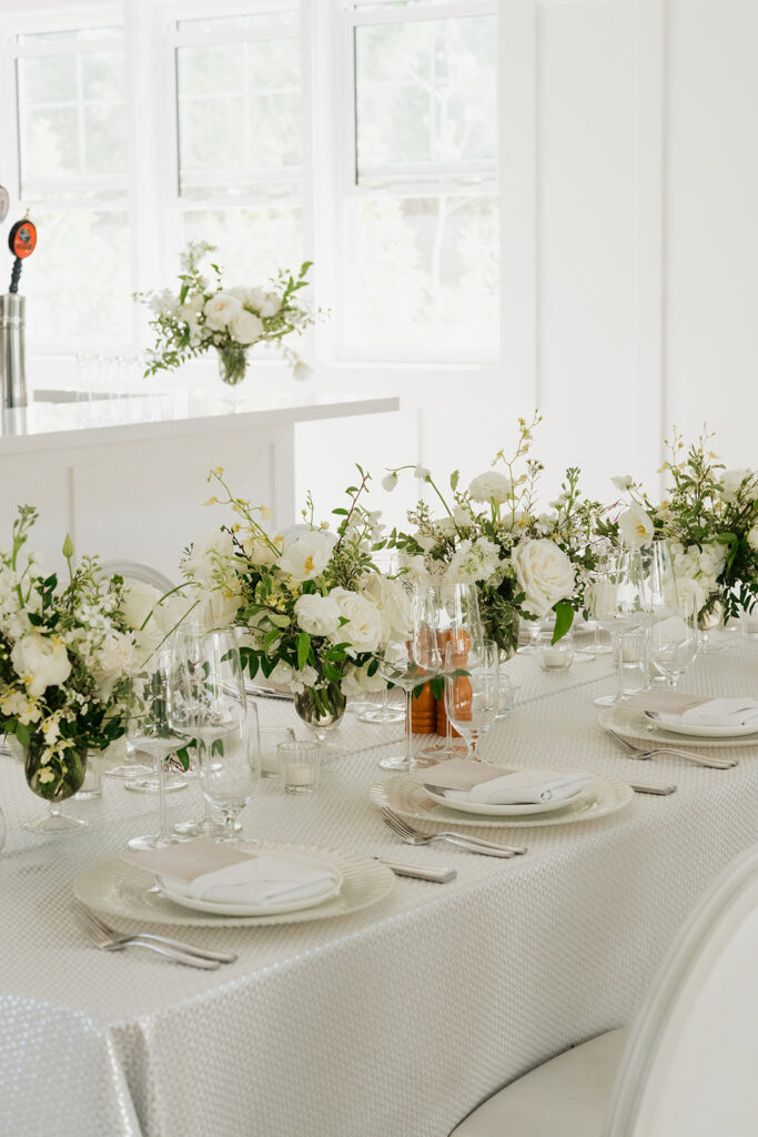 Ethereal white wedding reception with a breathtaking canopy of cascading white wisteria & green vines. Tables feature low, lush centerpieces combining garden roses, hydrangeas, spray roses, waxflower, delphinium, ranunculus, tulips, oncidium orchids, lisianthus, tweedia, lilac, sweet peas and are accented by deep-green foliage. This stunning floral design creates a luxurious, romantic, all-white atmosphere. Design by Rosemary & Finch Floral Design in Nashville, TN. 