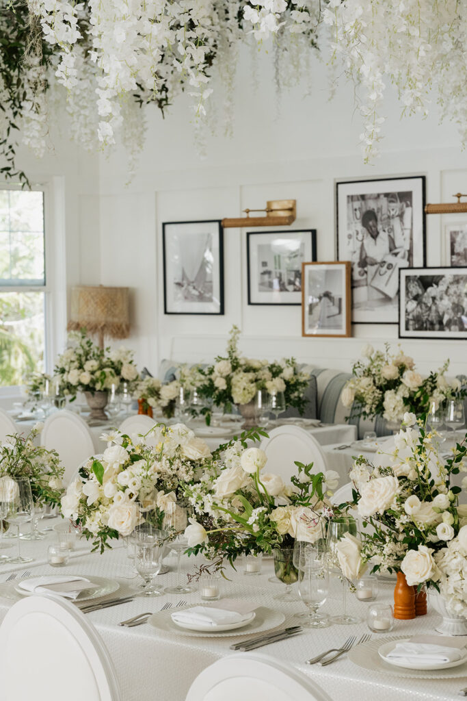 Ethereal white wedding reception with a breathtaking canopy of cascading white wisteria & green vines. Tables feature low, lush centerpieces combining garden roses, hydrangeas, spray roses, waxflower, delphinium, ranunculus, tulips, oncidium orchids, lisianthus, tweedia, lilac, sweet peas and are accented by deep-green foliage. This stunning floral design creates a luxurious, romantic, all-white atmosphere. Design by Rosemary & Finch Floral Design in Nashville, TN. 