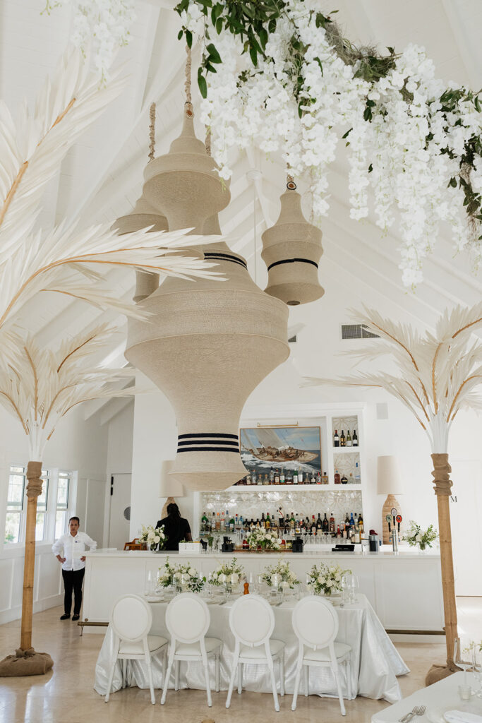 Ethereal white wedding reception with a breathtaking canopy of cascading white wisteria & green vines. Tables feature low, lush centerpieces combining garden roses, hydrangeas, spray roses, waxflower, delphinium, ranunculus, tulips, oncidium orchids, lisianthus, tweedia, lilac, sweet peas and are accented by deep-green foliage. This stunning floral design creates a luxurious, romantic, all-white atmosphere. Design by Rosemary & Finch Floral Design in Nashville, TN. 