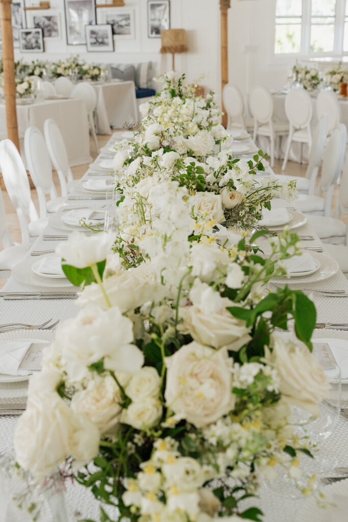Ethereal white wedding reception with a breathtaking canopy of cascading white wisteria & green vines. Tables feature low, lush centerpieces combining garden roses, hydrangeas, spray roses, waxflower, delphinium, ranunculus, tulips, oncidium orchids, lisianthus, tweedia, lilac, sweet peas and are accented by deep-green foliage. This stunning floral design creates a luxurious, romantic, all-white atmosphere. Design by Rosemary & Finch Floral Design in Nashville, TN. 