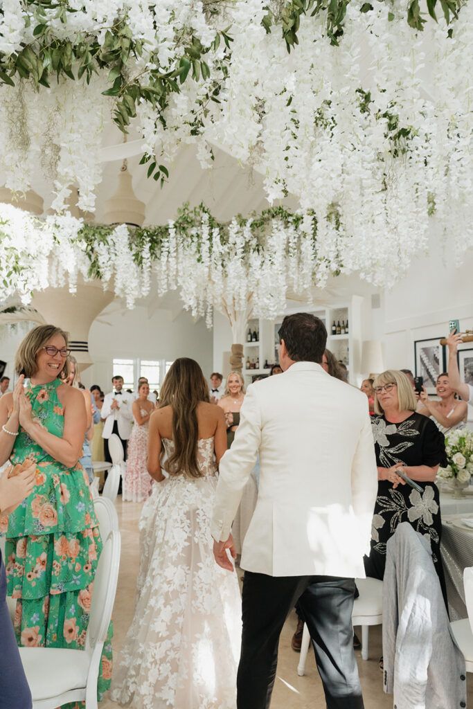 Ethereal white wedding reception with a breathtaking canopy of cascading white wisteria & green vines. Tables feature low, lush centerpieces combining garden roses, hydrangeas, spray roses, waxflower, delphinium, ranunculus, tulips, oncidium orchids, lisianthus, tweedia, lilac, sweet peas and are accented by deep-green foliage. This stunning floral design creates a luxurious, romantic, all-white atmosphere. Design by Rosemary & Finch Floral Design in Nashville, TN. 