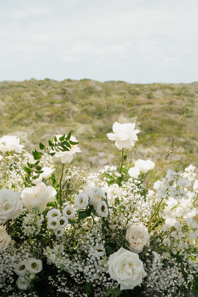 Simple, romantic all white floral bud vase arrangements for stunning bahamas cocktail hour. Bud vases are accompanied by all-white statement piece arrangements featuring garden roses, hydrangeas, spray roses, waxflower, delphinium, ranunculus, tulips, oncidium orchids, lisianthus, tweedia, lilac, sweet peas and are accented by a mix of greenery. Design by Rosemary & Finch Floral Design in Nashville, TN. 
