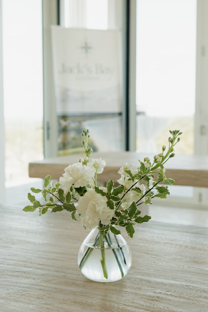 Simple, romantic all white floral bud vase arrangements for stunning bahamas cocktail hour. Bud vases are accompanied by all-white statement piece arrangements featuring garden roses, hydrangeas, spray roses, waxflower, delphinium, ranunculus, tulips, oncidium orchids, lisianthus, tweedia, lilac, sweet peas and are accented by a mix of greenery. Design by Rosemary & Finch Floral Design in Nashville, TN. 
