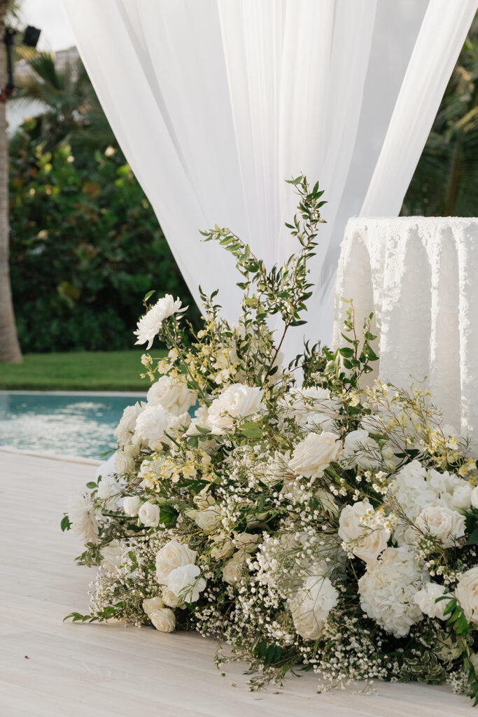Simple, romantic all white floral bud vase arrangements for stunning bahamas cocktail hour. Bud vases are accompanied by all-white statement piece arrangements featuring garden roses, hydrangeas, spray roses, waxflower, delphinium, ranunculus, tulips, oncidium orchids, lisianthus, tweedia, lilac, sweet peas and are accented by a mix of greenery. Design by Rosemary & Finch Floral Design in Nashville, TN. 
