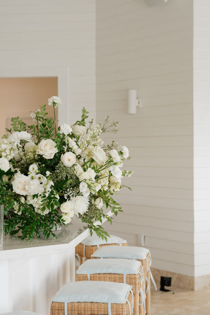 Simple, romantic all white floral bud vase arrangements for stunning bahamas cocktail hour. Bud vases are accompanied by all-white statement piece arrangements featuring garden roses, hydrangeas, spray roses, waxflower, delphinium, ranunculus, tulips, oncidium orchids, lisianthus, tweedia, lilac, sweet peas and are accented by a mix of greenery. Design by Rosemary & Finch Floral Design in Nashville, TN. 
