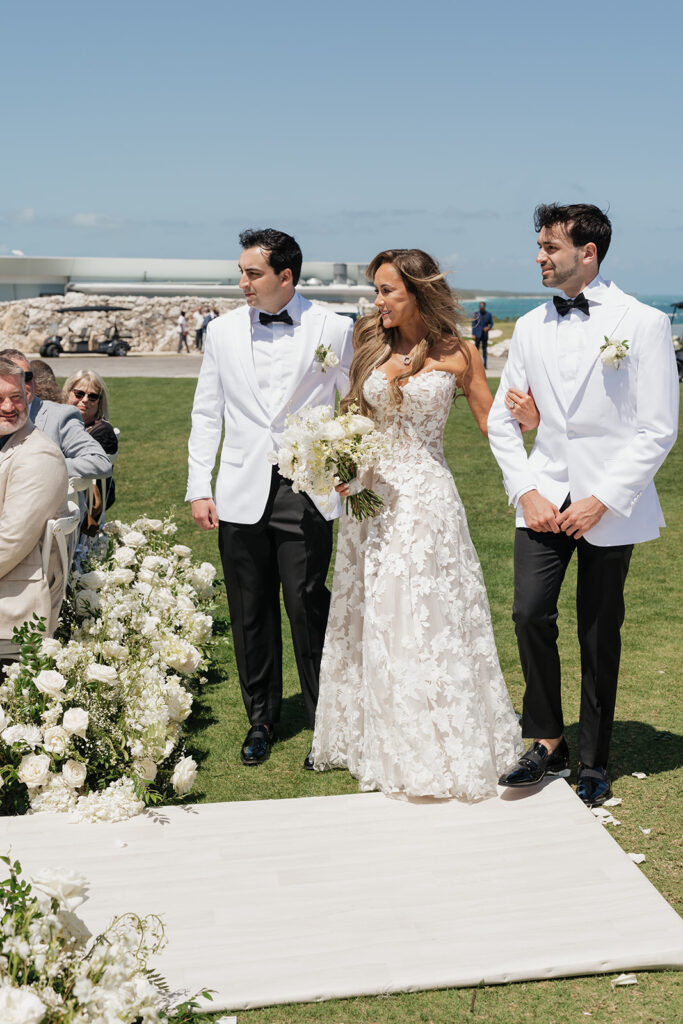 Lush white ceremony florals for a beachfront wedding in the Bahamas featuring garden roses, hydrangeas, delphinium, spray roses, baby’s breath, chrysanthemums, waxflower, carnations, tulips and a mixture of greens to create a refined and romantic aisle arrangement. Layered textures and soft movement give these all-white flowers an elevated, editorial look. Design by Rosemary & Finch Floral Design in Nashville, TN.