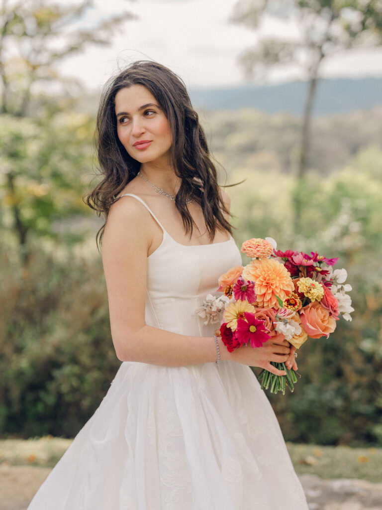 An autumnal, simple bridal bouquet displaying colors of burgundy, blush, rusty orange, and peach. Stunning florals include dahlias, garden roses, moab roses, cappuccino roses, brown ranunculus, zinnias, chocolate cosmos, brown sweet peas, toffee lisianthus, yarrow, marigolds and amaranthus. Beautiful fall florals for a wedding at Southall, TN. Design by Rosemary and Finch Floral Design in Nashville, TN.