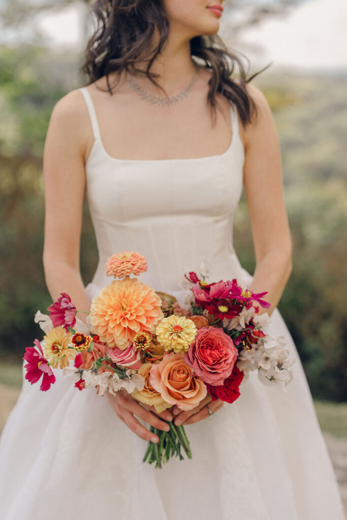 An autumnal, simple bridal bouquet displaying colors of burgundy, blush, rusty orange, and peach. Stunning florals include dahlias, garden roses, moab roses, cappuccino roses, brown ranunculus, zinnias, chocolate cosmos, brown sweet peas, toffee lisianthus, yarrow, marigolds and amaranthus. Beautiful fall florals for a wedding at Southall, TN. Design by Rosemary and Finch Floral Design in Nashville, TN.