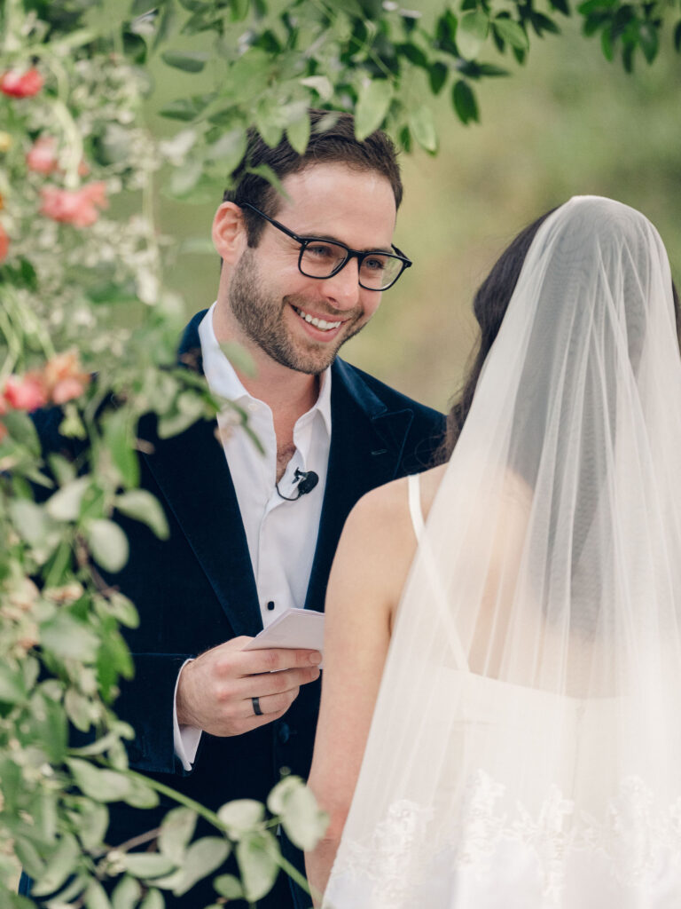 Stunning flower-forward, lush chuppah for fall wedding ceremony at Southall Farm and Inn. Bright, autumnal colors of rosy pink, deep red, blush, rusty orange, peach, and golden yellow are combined with the depth of full greenery. Color-blocked florals of dahlias, tess roses, cappuccino roses, moab roses, quicksand roses, spray roses, zinnias, lisianthus, yarrow, marigolds, ranunculus, and more cover the chuppah. Design by Rosemary and Finch Floral Design in Nashville, TN.