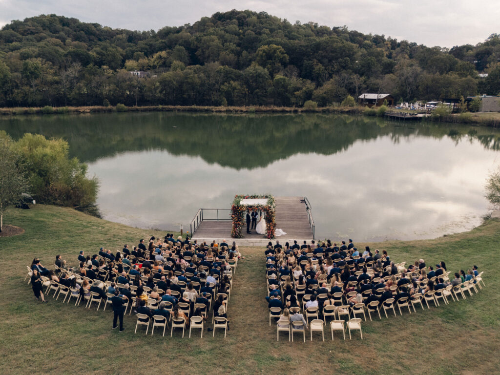 Stunning flower-forward, lush chuppah for fall wedding ceremony at Southall Farm and Inn. Bright, autumnal colors of rosy pink, deep red, blush, rusty orange, peach, and golden yellow are combined with the depth of full greenery. Color-blocked florals of dahlias, tess roses, cappuccino roses, moab roses, quicksand roses, spray roses, zinnias, lisianthus, yarrow, marigolds, ranunculus, and more cover the chuppah. Design by Rosemary and Finch Floral Design in Nashville, TN.