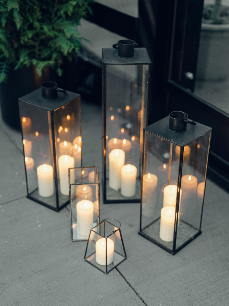 Elegant outdoor cocktail hour with bud vase floral arrangements scattered throughout high boy tables. All-white roses, lisianthus, delphinium, spray roses, ranunculus, campunala, saponaria, and light greenery were used for bud vases to correspond with floral reception centerpieces. The escort display was highlighted with chamomile, flannel flower, ranunculus, cloud garden roses, spray roses and greenery. Design by Rosemary and Finch Floral Design in Nashville, TN. 