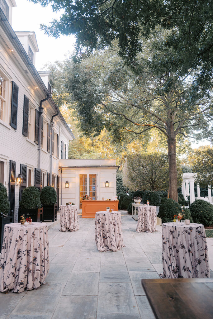 White ceramic bud vases with light florals scattered throughout cocktail hour for a private birthday party event in Nashville, TN. Bud vases consist of light greenery, peach dahlias, explosion grass, amber ranunculus, toffee lisianthus, copper zinnias, red marigolds, clematis pods, and nigella. Design by Rosemary and Finch Floral Design in Nashville, TN. 