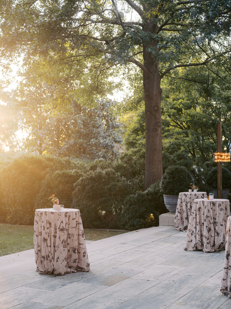 White ceramic bud vases with light florals scattered throughout cocktail hour for a private birthday party event in Nashville, TN. Bud vases consist of light greenery, peach dahlias, explosion grass, amber ranunculus, toffee lisianthus, copper zinnias, red marigolds, clematis pods, and nigella. Design by Rosemary and Finch Floral Design in Nashville, TN. 