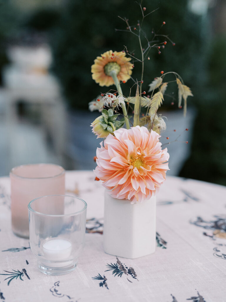 White ceramic bud vases with light florals scattered throughout cocktail hour for a private birthday party event in Nashville, TN. Bud vases consist of light greenery, peach dahlias, explosion grass, amber ranunculus, toffee lisianthus, copper zinnias, red marigolds, clematis pods, and nigella. Design by Rosemary and Finch Floral Design in Nashville, TN. 