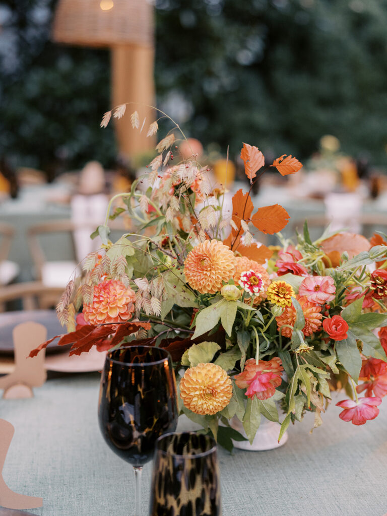 Gorgeous, flower-forward centerpiece arrangements for a private birthday party in Nashville, TN. Autumnal hues of red, brown, orange, pinks and cream are showcased in a stunning display of dahlias, zinnias, ranunculus, nigella, viburnum, rudbeckia, marigolds, liquid amber, spray roses, geranium, rose hips and bittersweet. Fall foliage provides greenery for arrangements and are wrapped around each tent pole and pendant. Design by Rosemary and Finch Floral Design in Nashville, TN. 