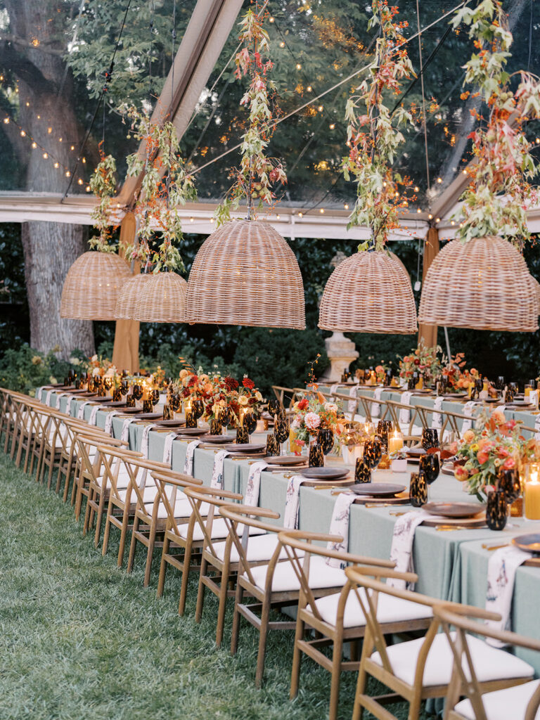 Gorgeous, flower-forward centerpiece arrangements for a private birthday party in Nashville, TN. Autumnal hues of red, brown, orange, pinks and cream are showcased in a stunning display of dahlias, zinnias, ranunculus, nigella, viburnum, rudbeckia, marigolds, liquid amber, spray roses, geranium, rose hips and bittersweet. Fall foliage provides greenery for arrangements and are wrapped around each tent pole and pendant. Design by Rosemary and Finch Floral Design in Nashville, TN. 