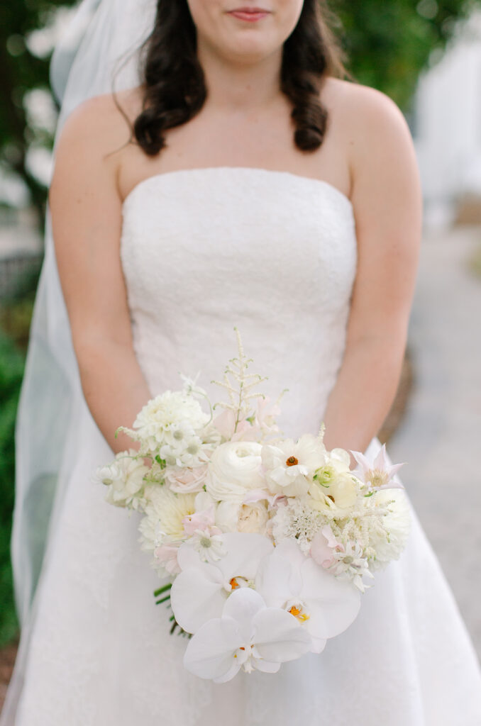 Stunning, elegant flower-forward all-white bridal bouquet with hints of blush and pink for Belle Meade wedding in Nashville. Florals highlighted are phalaenopsis, dahlias, garden roses, majolika roses, ranunculus, butterfly ranunculus, clematis, sweet peas, astilbe, scabiosa and light greenery. The white phalaenopsis creates a soft and bright focal moment for the bouquet. Design by Rosemary and Finch Floral Design in Nashville, TN. 