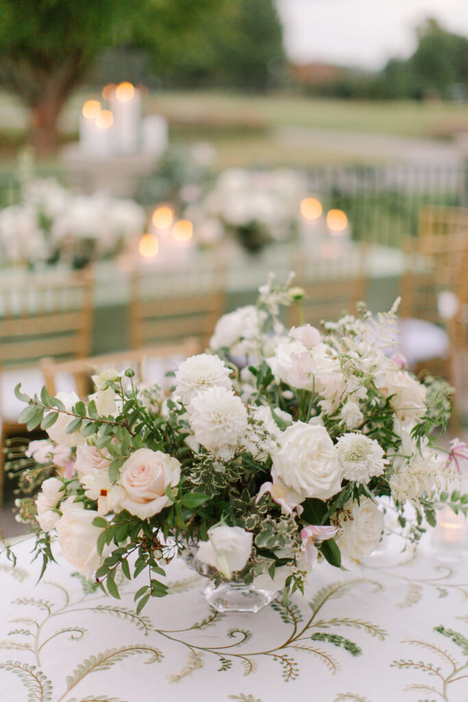 Lush and elegant floral centerpieces for Nashville wedding at Hillwood Country Club. Light pinks, blush and white florals consist of dahlias, garden roses, playa blancas, quicksand roses, ranunculus, lisianthus, majolikas, pieris, delphinium, sweet peas, saponaria, clematis, astilbe, and contrasting greenery. Centerpieces were accompanied by warm candlelight and lush vines growing near the bar for a beautiful wedding reception. Design by Rosemary and Finch Floral Design in Nashville, TN. 