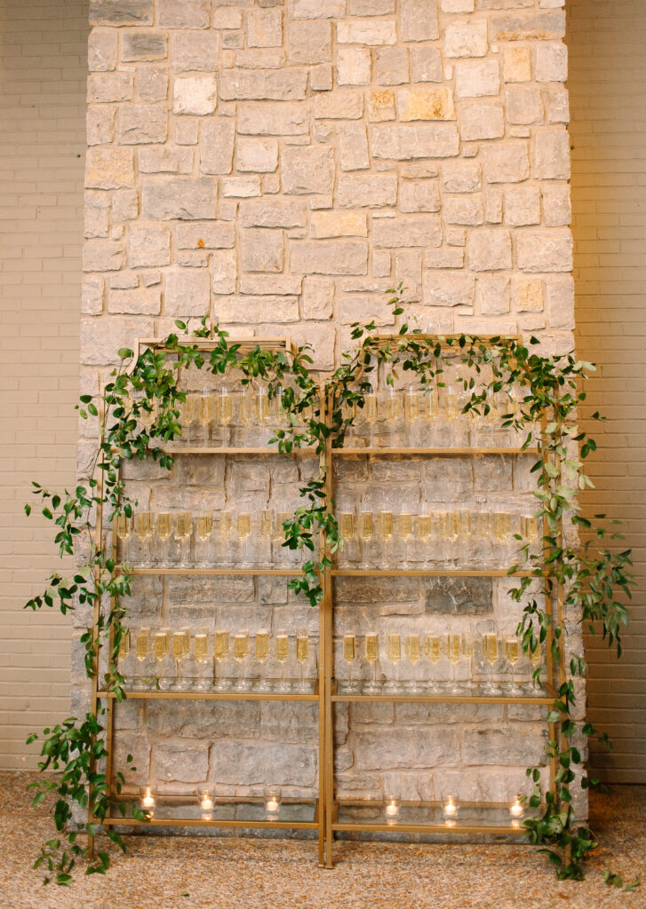 Stunning greenery is draped above and around the bar and reception area for a Nashville wedding at Hillwood Country Club. A wall of greenery adds to the elegance of the event and is accompanied by lush statement arrangements placed on the edge of the bar with all-white and blush florals consisting of dahlias, playa blancas, majolikas, garden roses, lisianthus, butterfly ranunculus, delphinium and more. Design by Rosemary and Finch Floral Design in Nashville, TN.