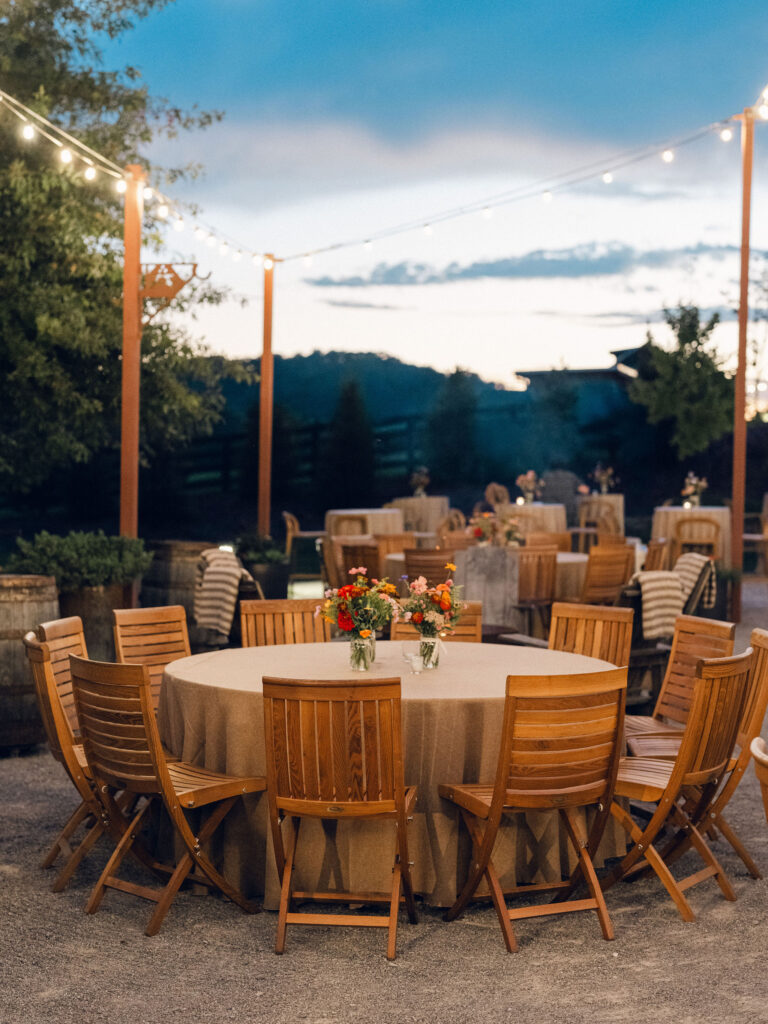 Simple, meadow-like arrangements are scattered on the tables for a southern themed welcome party at Southall Farm and Inn. The florals resemble bunches of wildflowers placed in glass jars and include cosmos, zinnias, cornflowers, yellow solidago riceflower and other wildflowers in an array of pinks, reds, yellows and oranges. Design by Rosemary and Finch Floral Design in Nashville, TN.
