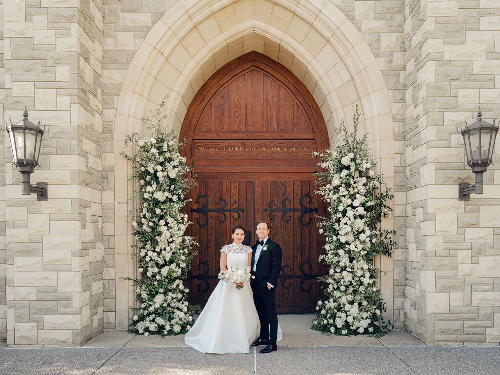 Stunning all-white floral arch for wedding ceremony at Covenant Presbyterian Church in Nashville. The arch creates an elegant focal point with flowers consisting of hydrangeas, cloud roses, lisianthus, ranunculus, tulips, dahlias, riceflower, stock, allium, delphinium, and ivy. Meadows with the same flowers surround the bottom of the arch on either side. Design by Rosemary & Finch Floral Design in Nashville, TN.