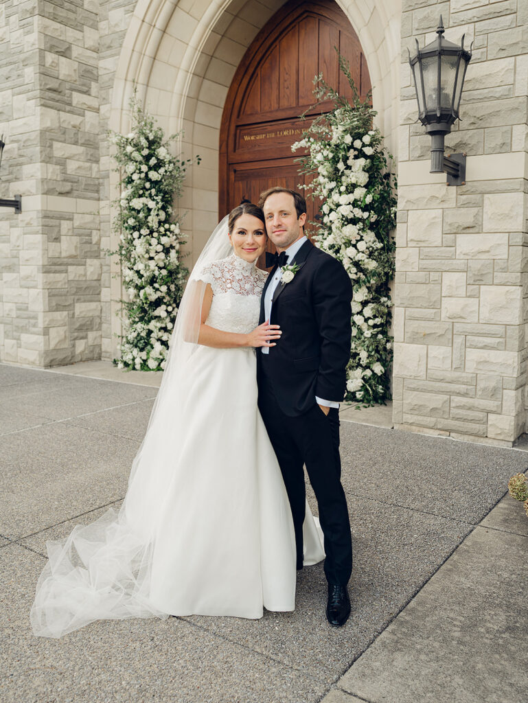 Stunning all-white floral arch for wedding ceremony at Covenant Presbyterian Church in Nashville. The arch creates an elegant focal point with flowers consisting of hydrangeas, cloud roses, lisianthus, ranunculus, tulips, dahlias, riceflower, stock, allium, delphinium, and ivy. Meadows with the same flowers surround the bottom of the arch on either side. Design by Rosemary & Finch Floral Design in Nashville, TN.