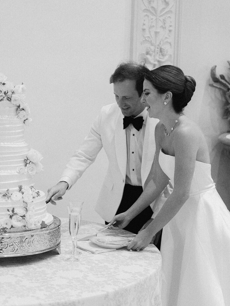 Simple, all-white florals cascade down the side of stunning reception wedding cake. Spray roses, cloud roses, ranunculus, riceflower, olive branches and ivy are used to create a beautiful cake display. Design by Rosemary & Finch Floral Design in Nashville, TN.