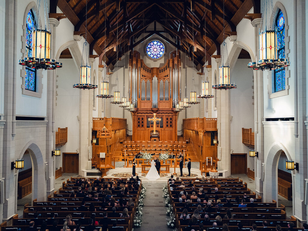 Romantic and elegant aisle meadows are highlighted with all-white garden roses, hydrangeas, spray roses, riceflower, stock and delphinium. Light greenery, including olive branches, create a soft contrast to the meadows. Stunning sanctuary aisle meadows that are repurposed to the dance floor stage meadows. Statement urns at the altar consist of the same flowers and offer a stunning focal point for the ceremony. Design by Rosemary & Finch Floral Design in Nashville, TN.
