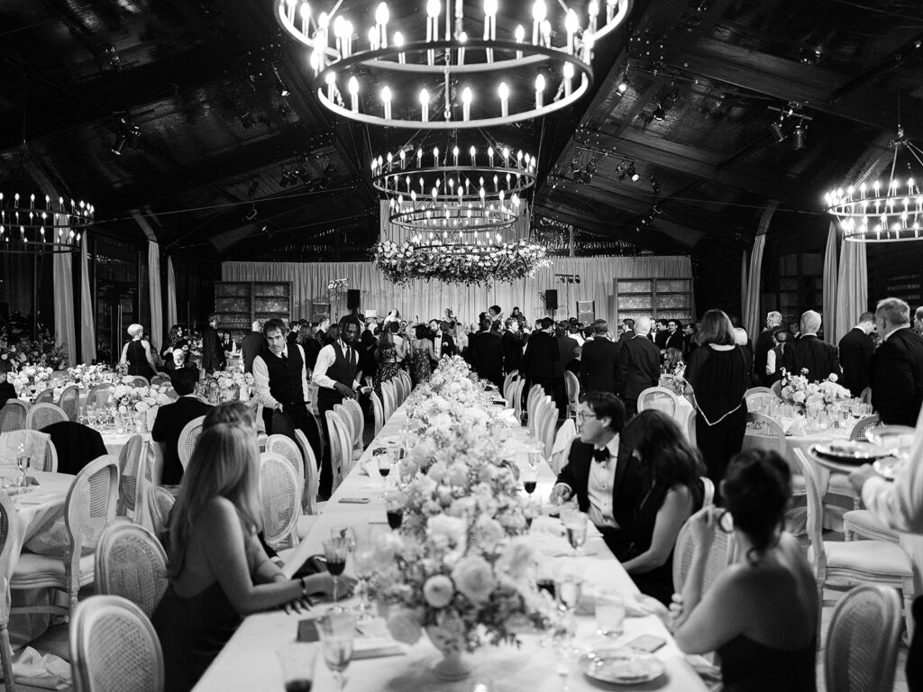 Romantic and stunning glass-tented wedding reception at Cheekwood botanical garden in Nashville, TN. Elegant garden-inspired centerpieces feature lush, all-white cloud roses, hydrangeas, lisianthus, dahlias, sweet peas, double tulips, delphinium, stock, allium, flowering champagne, and more with light greenery. Matching banquette meadows line either side of the glass tent creating a lush and timeless feel. Design by Rosemary & Finch Floral Design in Nashville, TN.