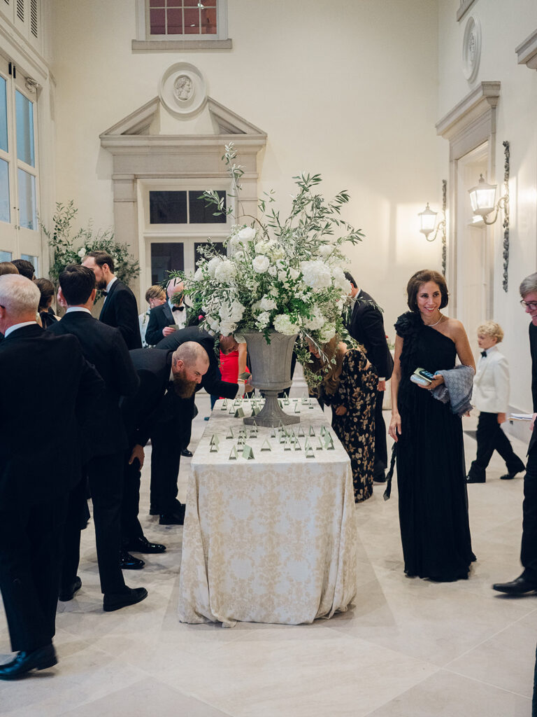 Soft, elegant floral statements create a stunning focal point for guests as they enter a glass-tented reception. All-white hydrangeas, lisianthus, cloud roses, spray roses, delphinium, stock, sweet peas, and dahlias spill over the sides of a loggia fountain. A large statement urn with all-white florals matching the fountain creates an extravagant moment for the escort display table. Design by Rosemary & Finch Floral Design in Nashville, TN.