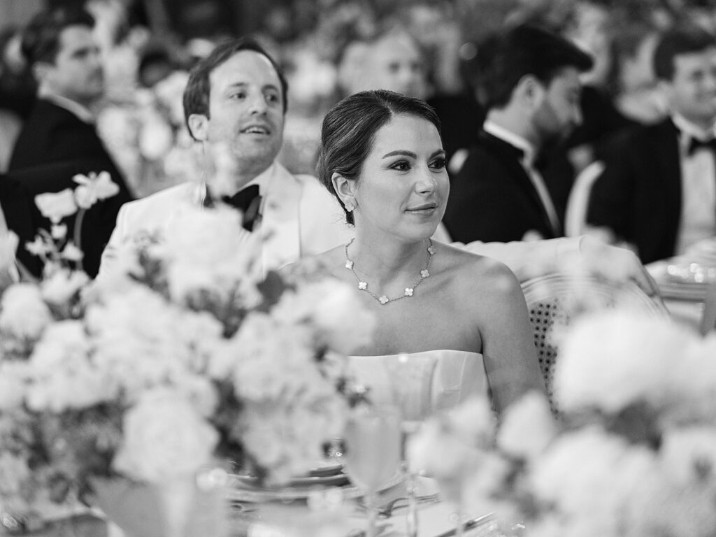 Romantic and stunning glass-tented wedding reception at Cheekwood botanical garden in Nashville, TN. Elegant garden-inspired centerpieces feature lush, all-white cloud roses, hydrangeas, lisianthus, dahlias, sweet peas, double tulips, delphinium, stock, allium, flowering champagne, and more with light greenery. Matching banquette meadows line either side of the glass tent creating a lush and timeless feel. Design by Rosemary & Finch Floral Design in Nashville, TN.