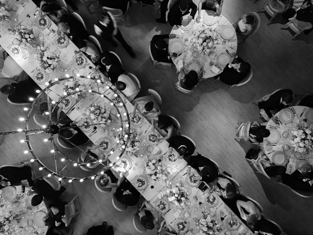 Romantic and stunning glass-tented wedding reception at Cheekwood botanical garden in Nashville, TN. Elegant garden-inspired centerpieces feature lush, all-white cloud roses, hydrangeas, lisianthus, dahlias, sweet peas, double tulips, delphinium, stock, allium, flowering champagne, and more with light greenery. Matching banquette meadows line either side of the glass tent creating a lush and timeless feel. Design by Rosemary & Finch Floral Design in Nashville, TN.