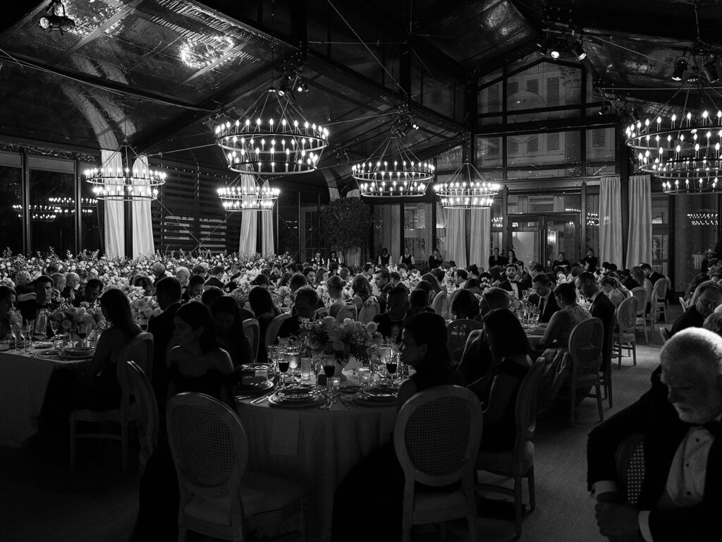 Romantic and stunning glass-tented wedding reception at Cheekwood botanical garden in Nashville, TN. Elegant garden-inspired centerpieces feature lush, all-white cloud roses, hydrangeas, lisianthus, dahlias, sweet peas, double tulips, delphinium, stock, allium, flowering champagne, and more with light greenery. Matching banquette meadows line either side of the glass tent creating a lush and timeless feel. Design by Rosemary & Finch Floral Design in Nashville, TN.