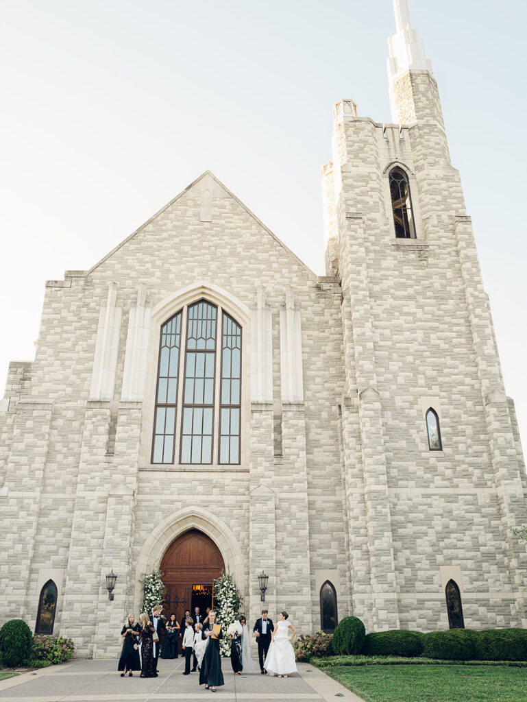 Stunning all-white floral arch for wedding ceremony at Covenant Presbyterian Church in Nashville. The arch creates an elegant focal point with flowers consisting of hydrangeas, cloud roses, lisianthus, ranunculus, tulips, dahlias, riceflower, stock, allium, delphinium, and ivy. Meadows with the same flowers surround the bottom of the arch on either side. Design by Rosemary & Finch Floral Design in Nashville, TN.
