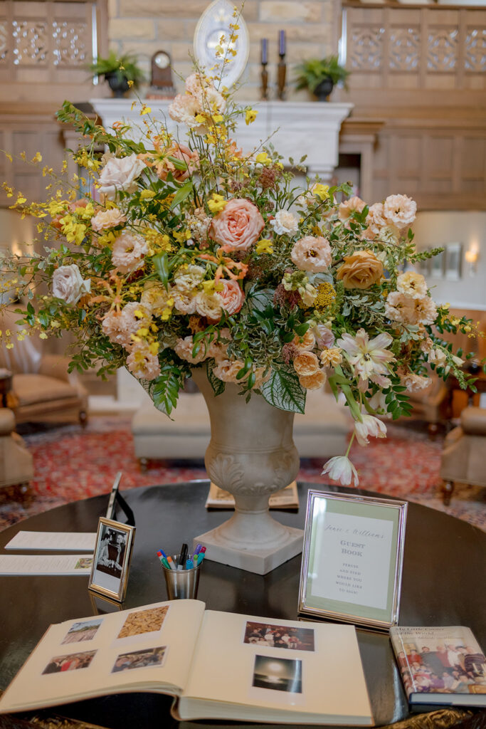 Stunning reception and bar statement arrangements catch the eye of guests at Sewanee, TN wedding. Colorful bursts of garden roses, moab roses, creme de la creme, carnations, spray roses, dahlias, tulips, yarrow, foxglove, zinnias, oncidium orchids, cosmos, smokebush and more are accompanied by soft greens and ferns. Arrangements are drenched in colors of peach, pinks, yellows and green. Design by Rosemary and Finch Floral Design in Nashville, TN. 