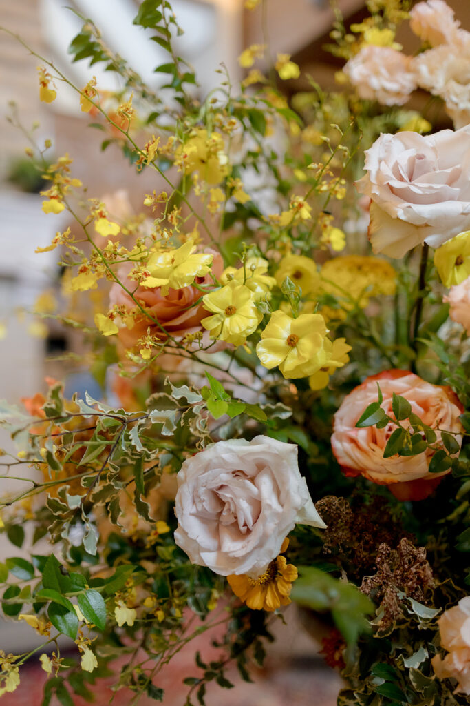 Stunning reception and bar statement arrangements catch the eye of guests at Sewanee, TN wedding. Colorful bursts of garden roses, moab roses, creme de la creme, carnations, spray roses, dahlias, tulips, yarrow, foxglove, zinnias, oncidium orchids, cosmos, smokebush and more are accompanied by soft greens and ferns. Arrangements are drenched in colors of peach, pinks, yellows and green. Design by Rosemary and Finch Floral Design in Nashville, TN. 