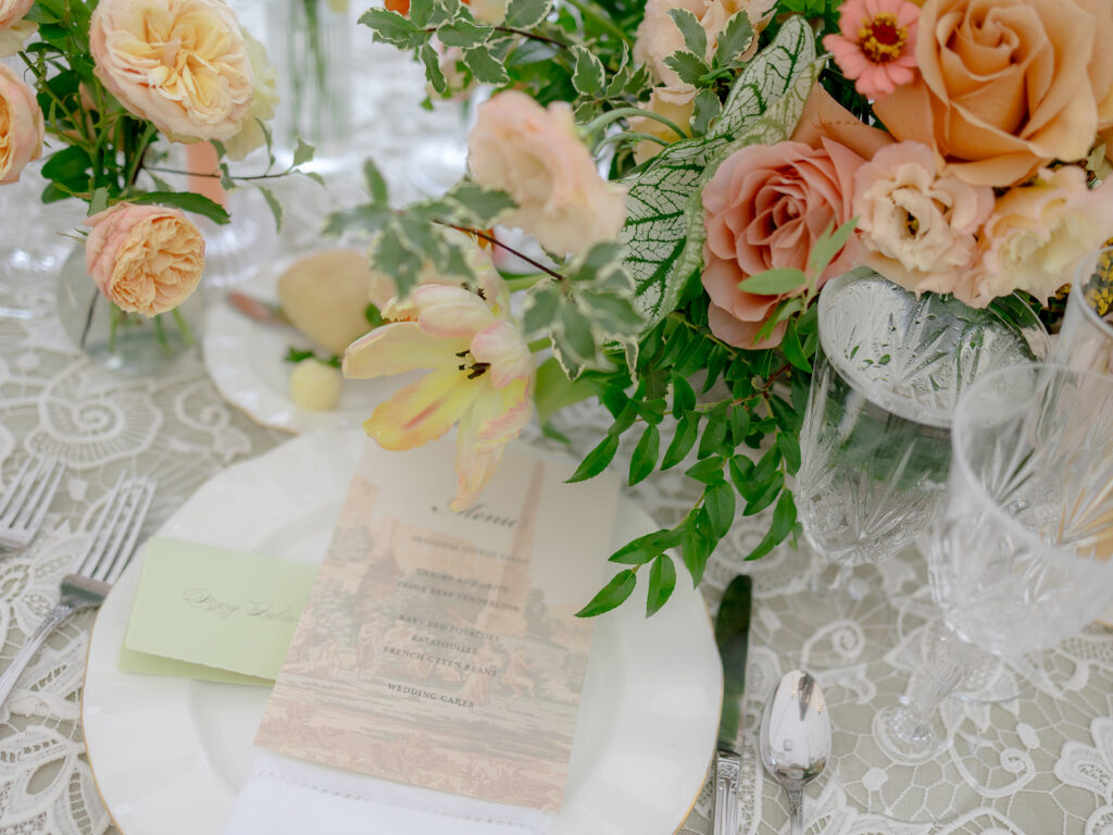 A mix of lush, garden-like floral centerpieces create a colorful display across tables under a canvas tent for a Sewanee wedding reception. Compotes, bud vases and ikebana arrangements overflow with garden roses, moab roses, icelandic poppies, lisianthus, tulips, dahlias, ranunculus, scabiosa, zinnias, sweet peas, oncidium and more in shades of peach, red, apricot and yellow. Lush greenery is suspended around light pendants under the tent. Design by Rosemary and Finch Floral Design in Nashville, TN.
