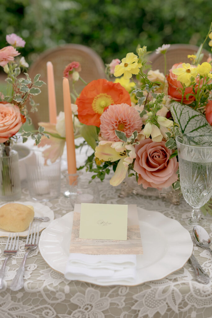 A mix of lush, garden-like floral centerpieces create a colorful display across tables under a canvas tent for a Sewanee wedding reception. Compotes, bud vases and ikebana arrangements overflow with garden roses, moab roses, icelandic poppies, lisianthus, tulips, dahlias, ranunculus, scabiosa, zinnias, sweet peas, oncidium and more in shades of peach, red, apricot and yellow. Lush greenery is suspended around light pendants under the tent. Design by Rosemary and Finch Floral Design in Nashville, TN.
