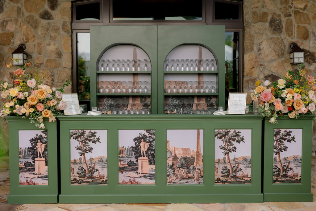 Stunning reception and bar statement arrangements catch the eye of guests at Sewanee, TN wedding. Colorful bursts of garden roses, moab roses, creme de la creme, carnations, spray roses, dahlias, tulips, yarrow, foxglove, zinnias, oncidium orchids, cosmos, smokebush and more are accompanied by soft greens and ferns. Arrangements are drenched in colors of peach, pinks, yellows and green. Design by Rosemary and Finch Floral Design in Nashville, TN. 