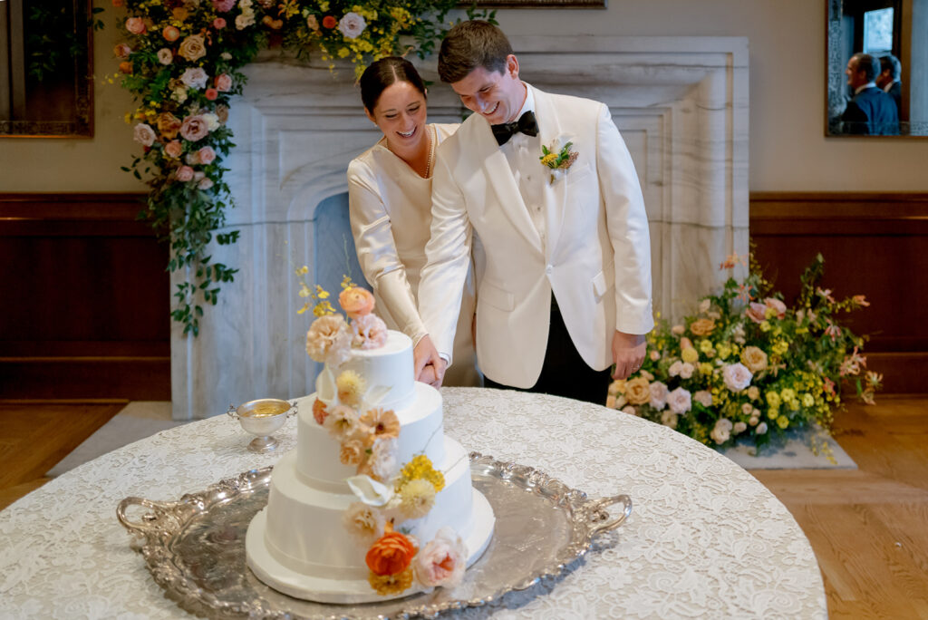 Stunning floral installation with bright colors of yellow, peach, blush, and green, perfectly frame fireplace in the Sewanee Inn. Flowers highlighted are garden roses, spray roses, moab roses, butterfly ranunculus, ranunculus, lisianthus, zinnias, foxglove, gloriosa, oncidium, smokebush,  cottage yarrow, carnations, tulips and greenery including smilax. The wedding cake florals are also highlighted near the fireplace. Design by Rosemary and Finch Floral Design in Nashville, TN.