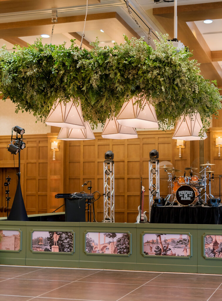 A lush, all-green dance floor installation is suspended in the air surrounding large light pendants. Featuring smilax, huckleberry branches and mini pitt greens, the dance floor has a moody yet lively focal point for guests to enjoy and dance under. Design by Rosemary and Finch Floral Design in Nashville, TN.